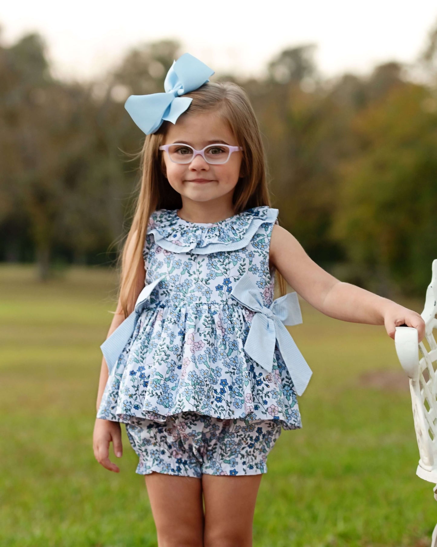 Young girl in a floral dress with a large blue bow outdoors