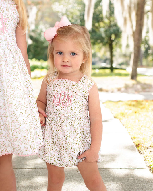 Young girl in a floral dress with a pink bow standing outdoors.