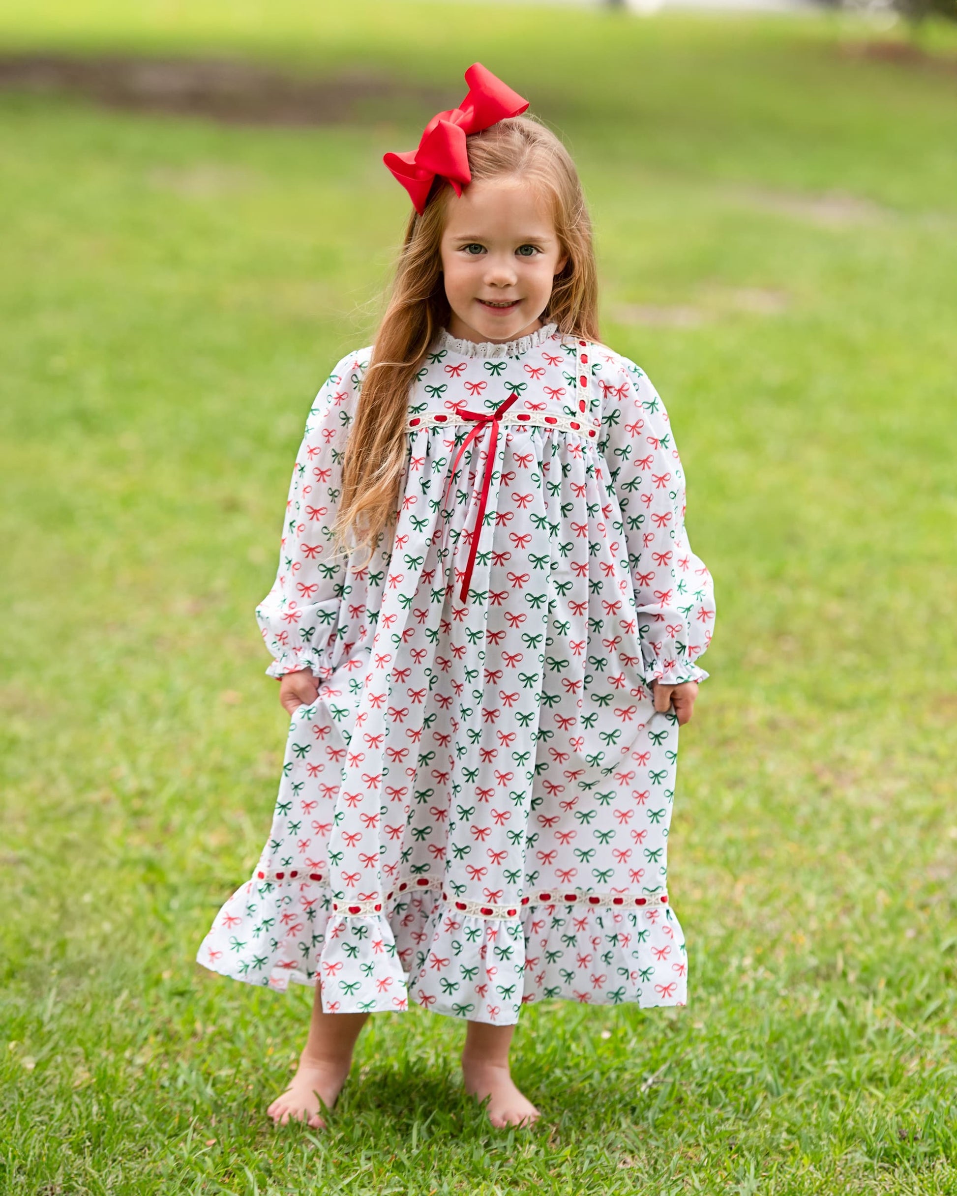 Young girl in a floral dress with a red bow standing on grass