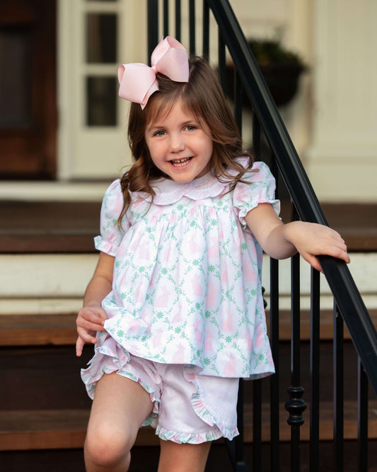 Young girl in a floral outfit with a large pink bow standing on a staircase.