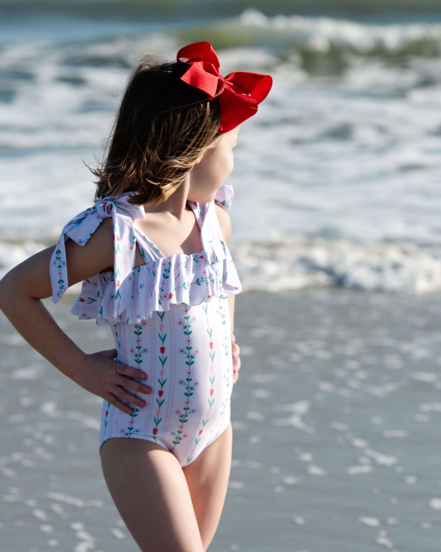 Young girl in a floral swimsuit with a red bow on a beach