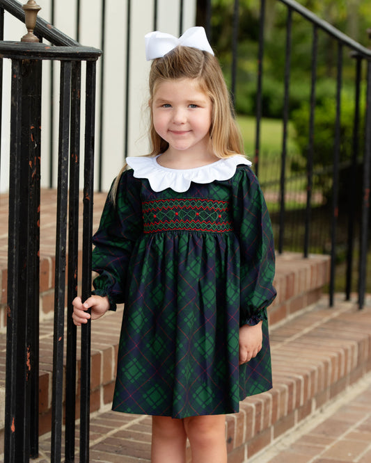Young girl in a green and black checkered dress with a white collar standing on a staircase.