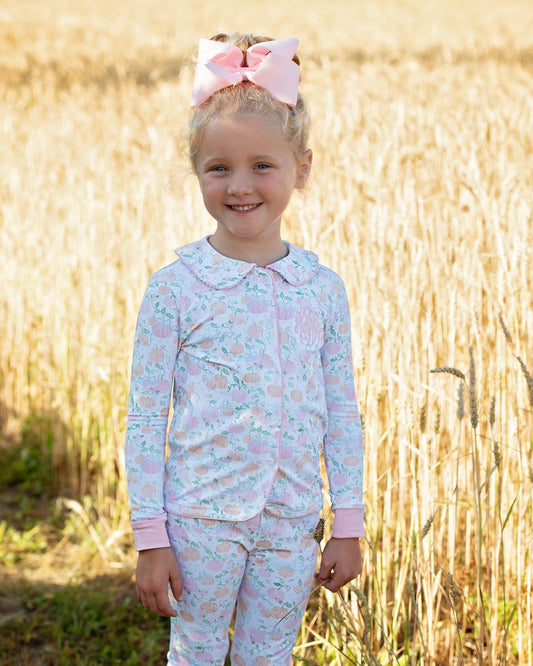 Young girl in a light blue and pink pajama set with a pink bow standing in a field.