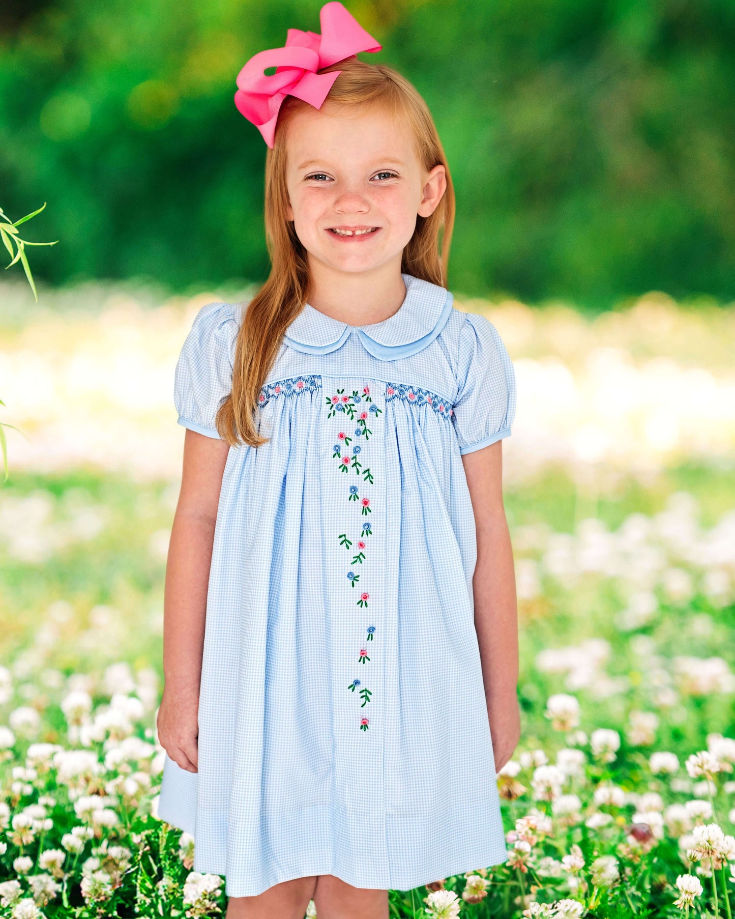 Young girl in a light blue dress with floral embroidery standing in a field of flowers.