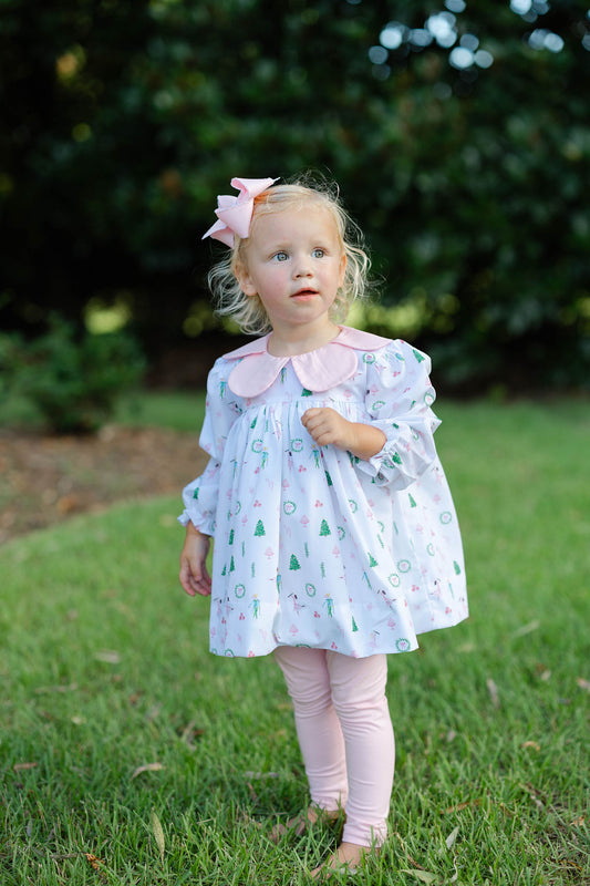 Young girl in a patterned dress standing on grass with greenery in the background