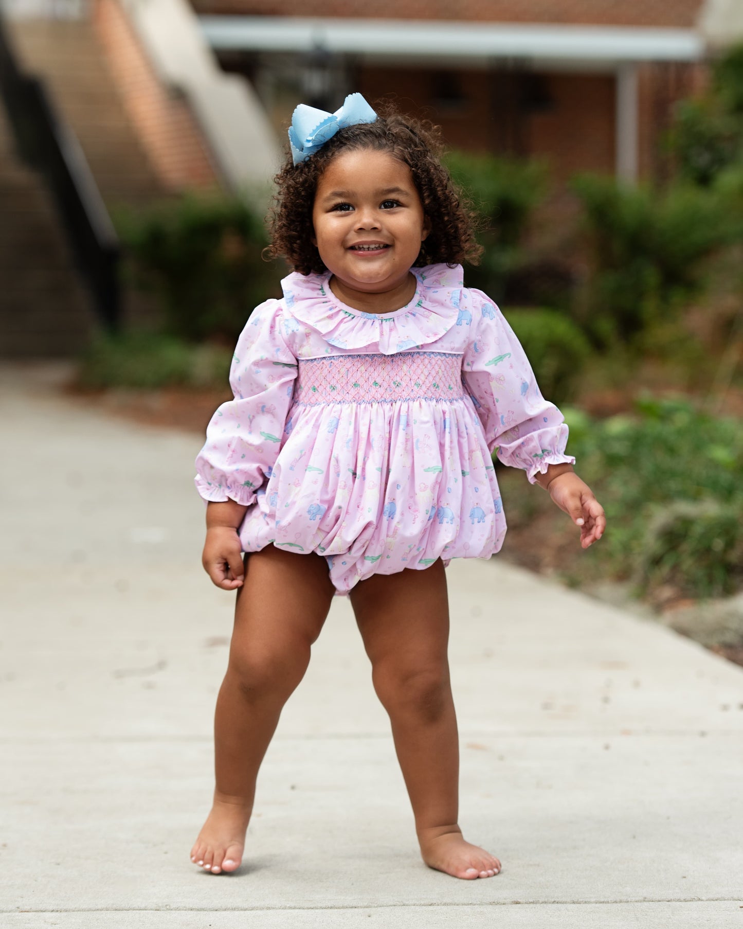 Young girl in a pink dress with ruffles standing on a wooden deck.