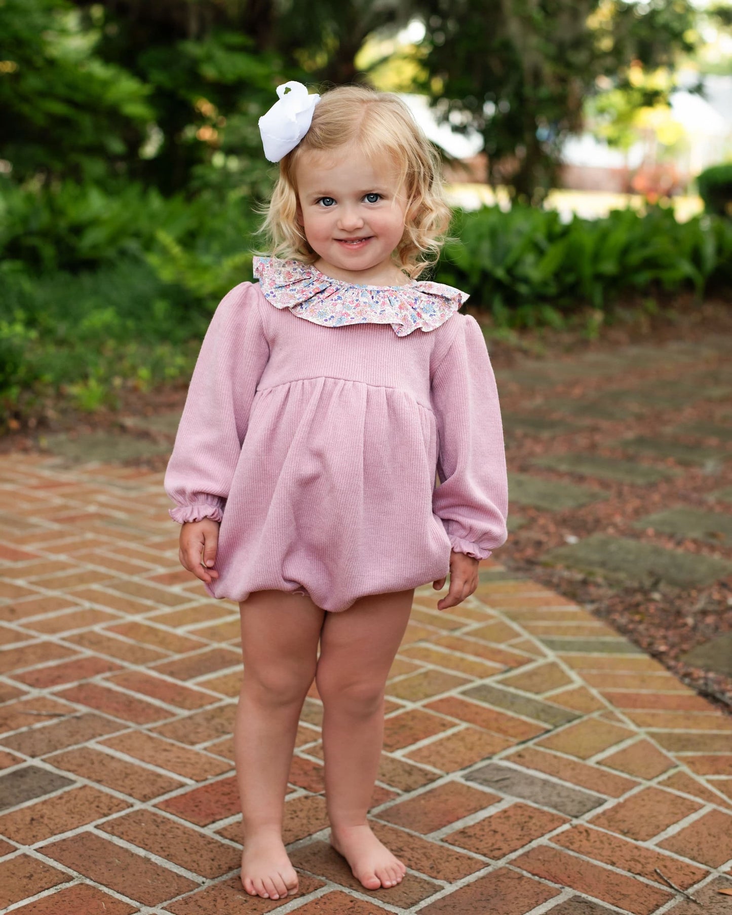 Young girl in a pink bubble with a floral collar standing on a brick path.