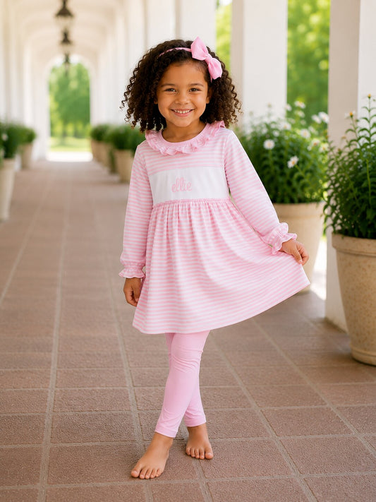 Young girl in a pink dress and leggings standing on a tiled patio with plants in the background.