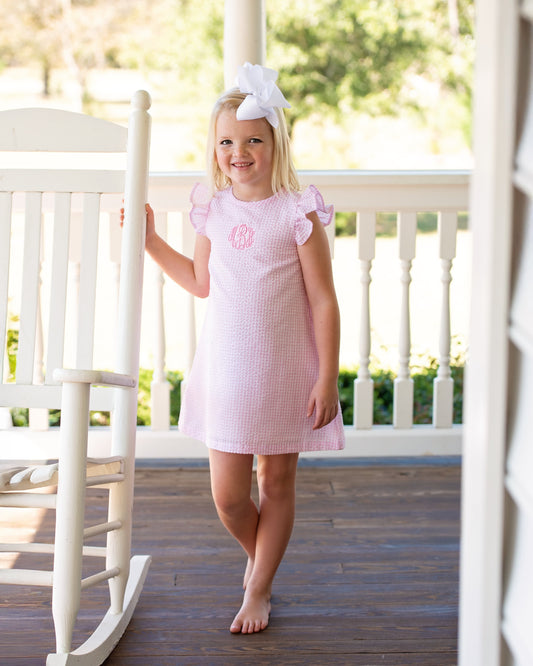 Young girl in a pink dress standing on a porch with a white rocking chair.