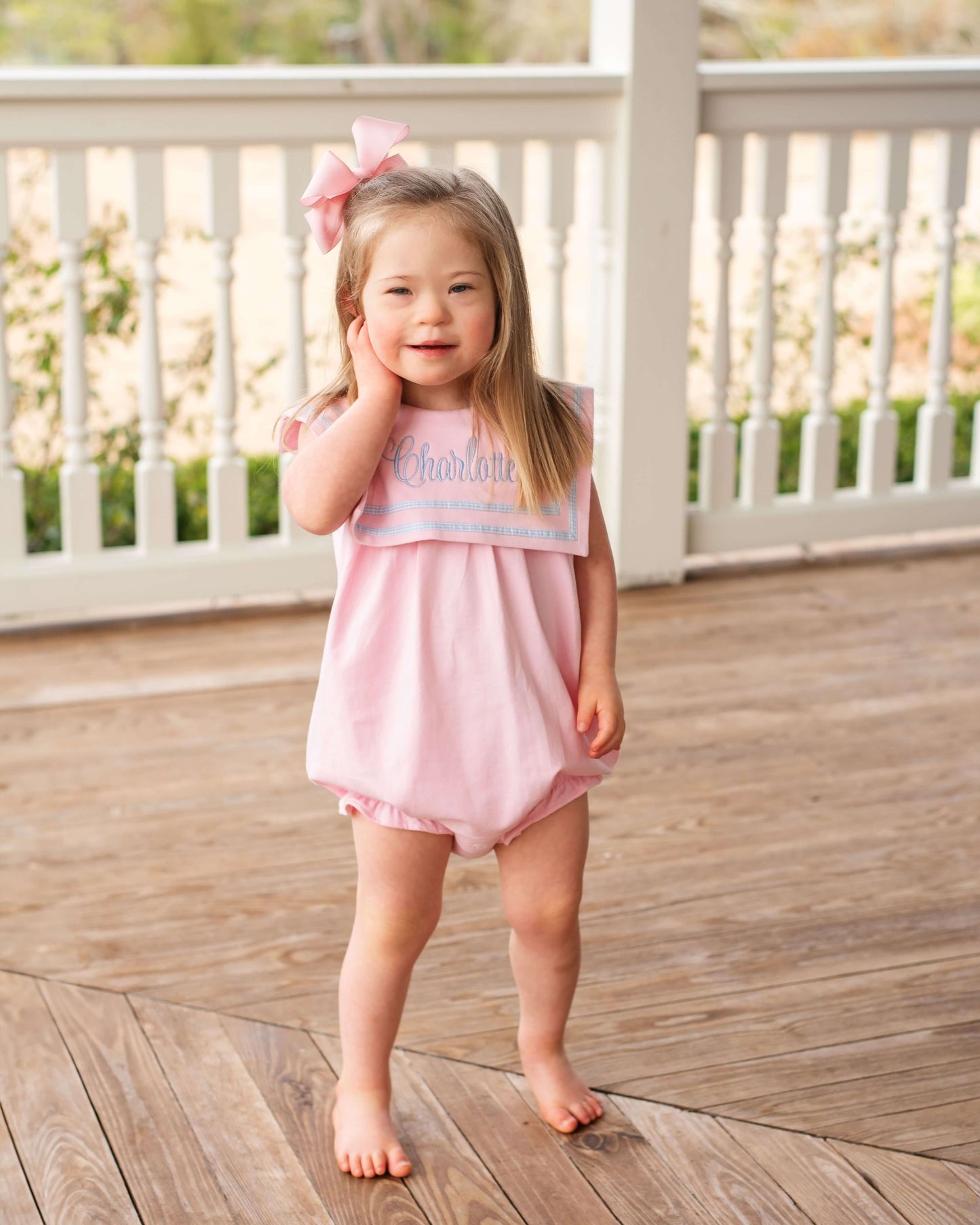 Young girl in a pink dress standing on a wooden deck.