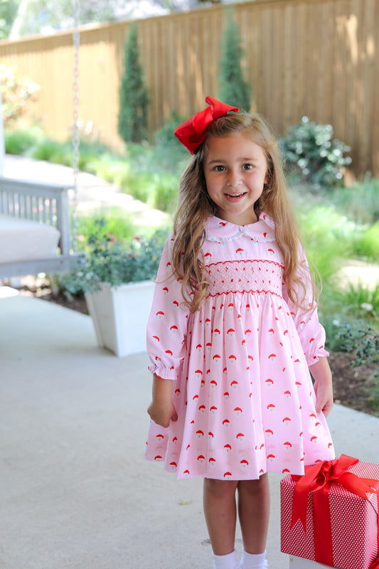 Young girl in a pink dress with a red bow, holding a red gift box outdoors.