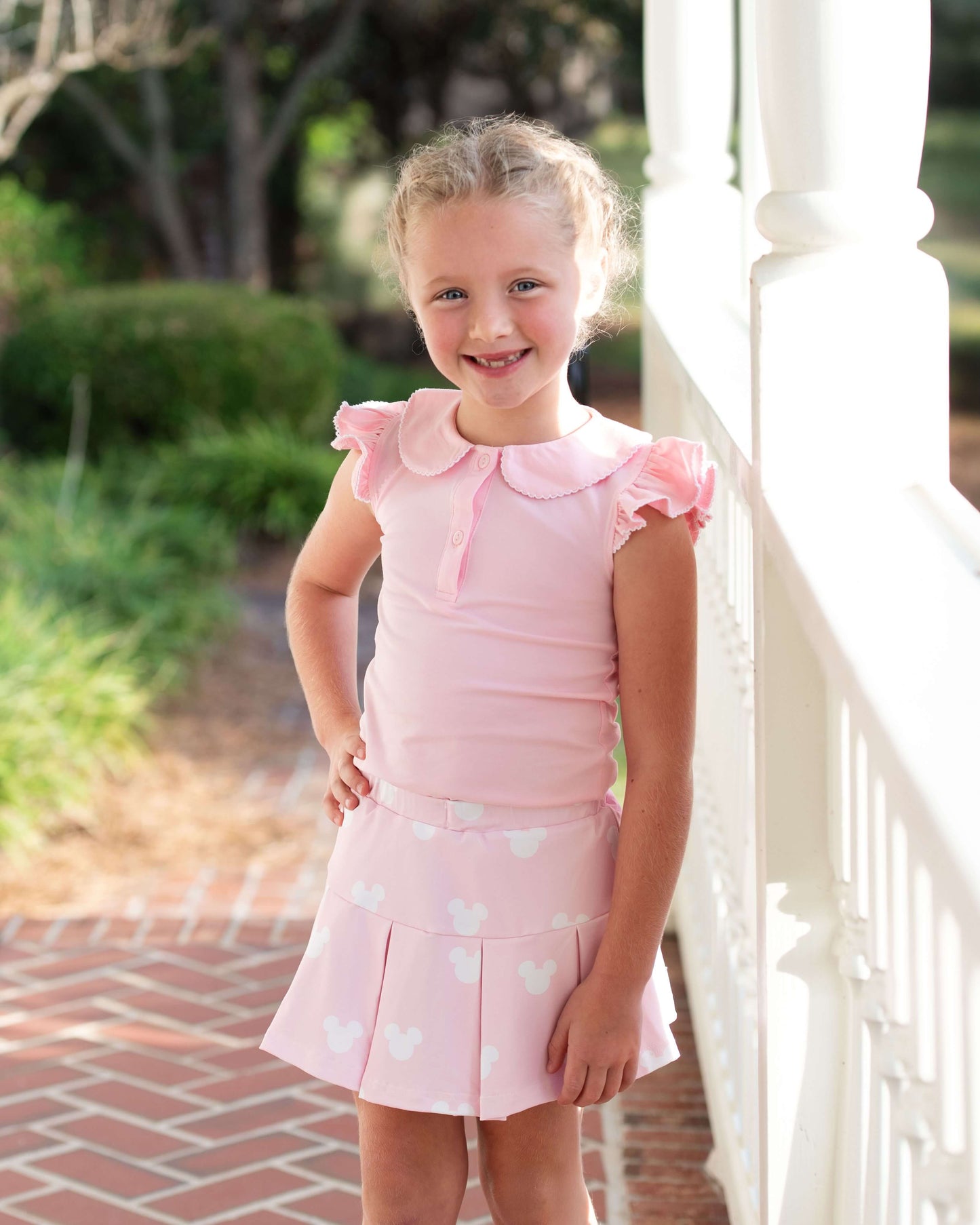 Young girl in a pink dress with heart patterns standing outdoors.