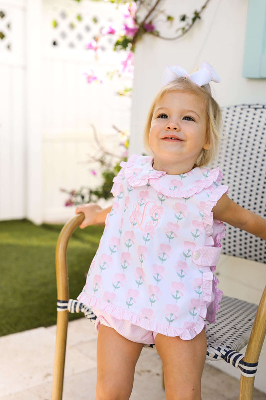 Young girl in a pink floral outfit standing outdoors.