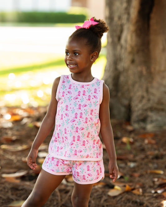 Young girl in a pink floral outfit standing outdoors near a tree