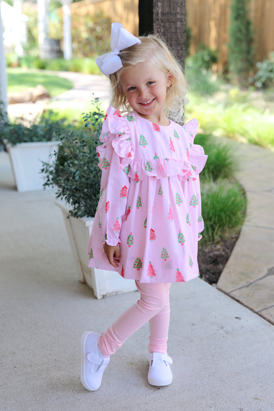 Young girl in a pink legging set with ruffles and a white bow outdoors.