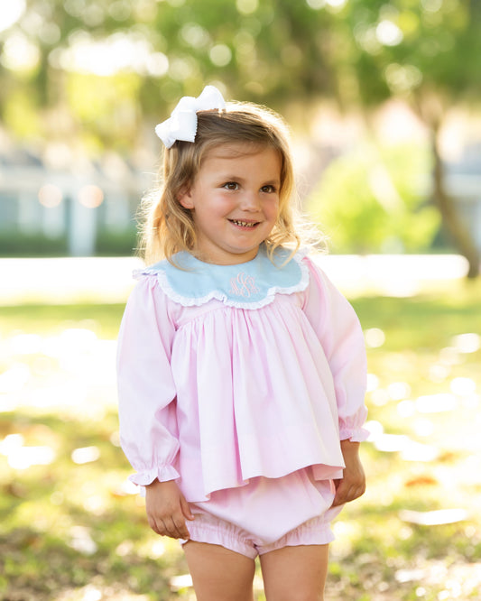 Young girl in a pink outfit with a blue collar standing outdoors.