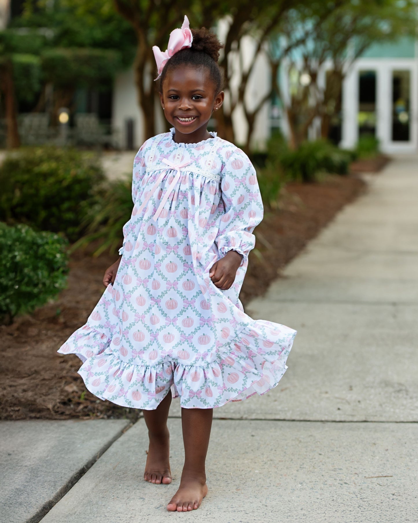 Young girl in a pumpkin night gown standing on a sidewalk with trees and bushes in the background 2