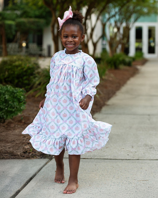 Young girl in a pumpkin night gown standing on a sidewalk with trees and bushes in the background 2