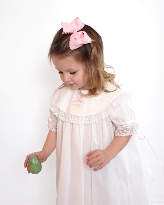 Young girl in a white dress with lace details holding a green object against a white background