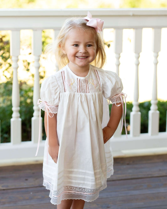 Young girl in a white dress with lace details standing on a wooden deck.