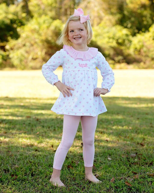 Young girl in a white dress with pink accents standing on grass