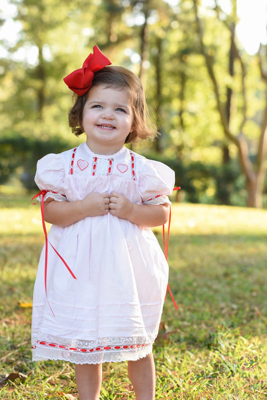 Young girl in a white dress with red accents standing outdoors in a park.