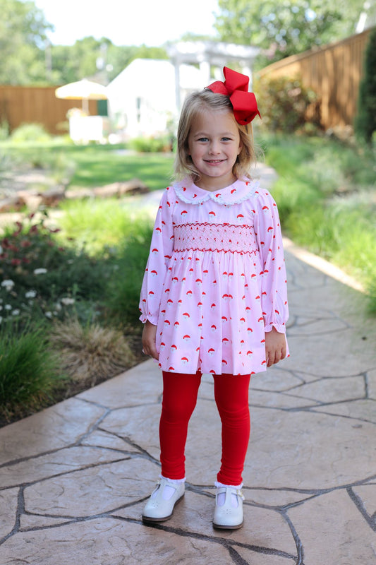 Young girl in a white dress with red patterns and red leggings standing on a stone path outdoors.