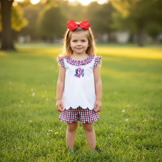Young girl in a white dress with red, white, and blue accents standing in a grassy field.