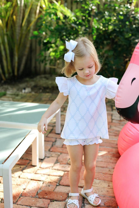 Young girl in a white outfit standing outdoors with pink balloons in the background