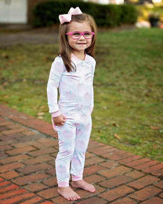 Young girl in a white outfit with pink and blue pumpkins on a brick path.
