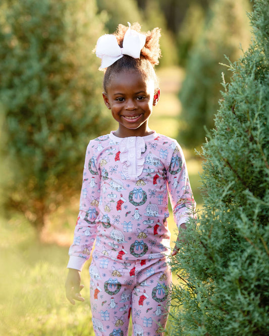 Young girl in pink pajamas with Christmas patterns standing in a tree lot.