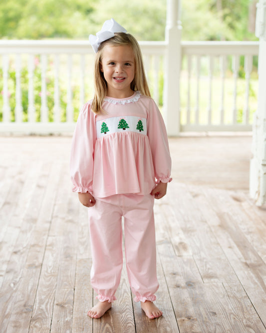 Young girl in pink pajamas with a white bow on a wooden porch