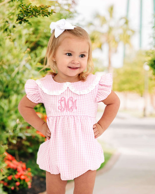 Young girl standing outside wearing a pink gingham bubble and white bow in her hair