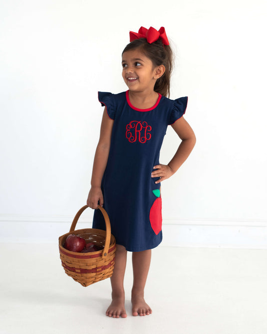 Young girl wearing a basket with apples in it wearing a navy dress with an applique apple.