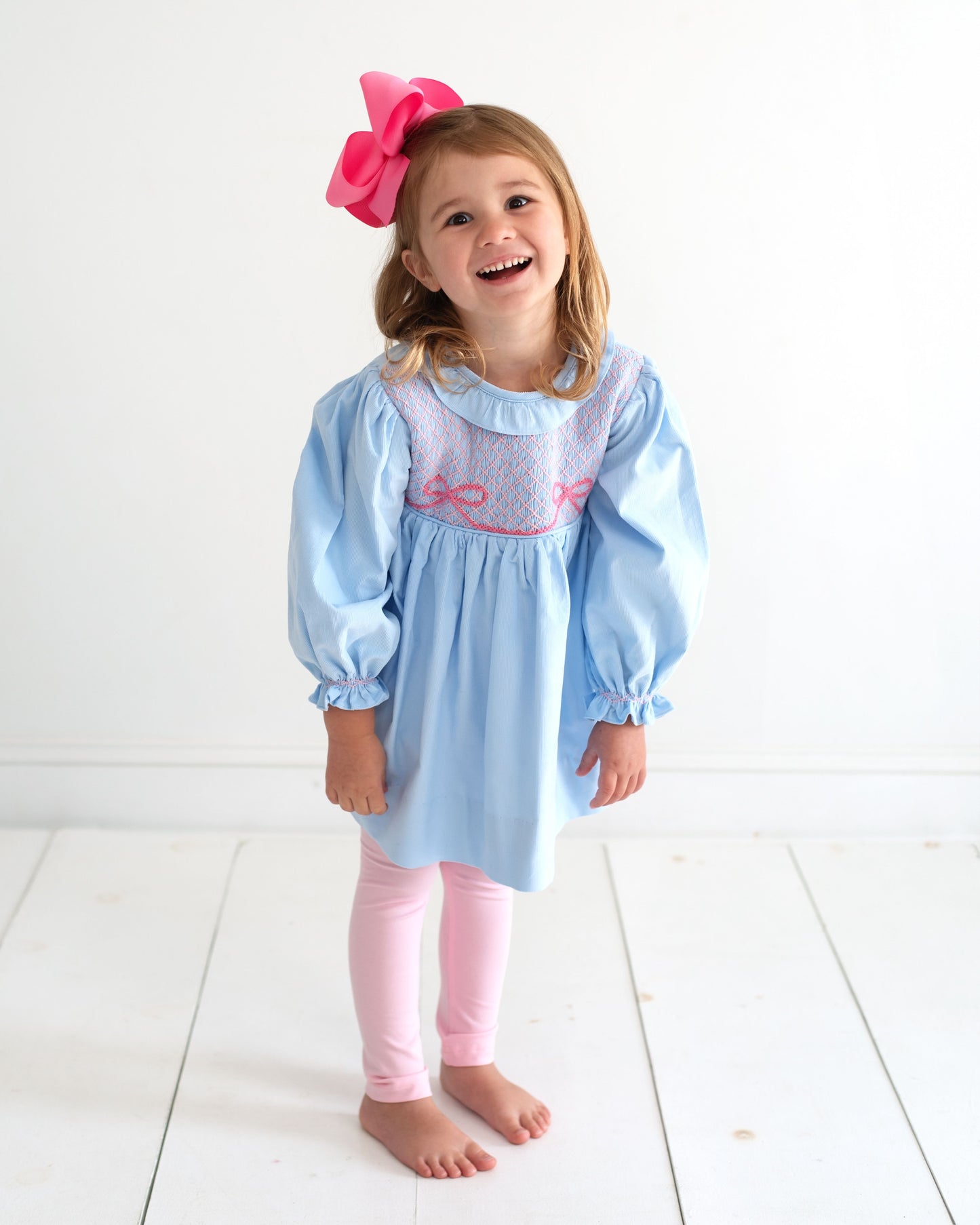 Young girl wearing a blue and pink legging set standing on a white floor.