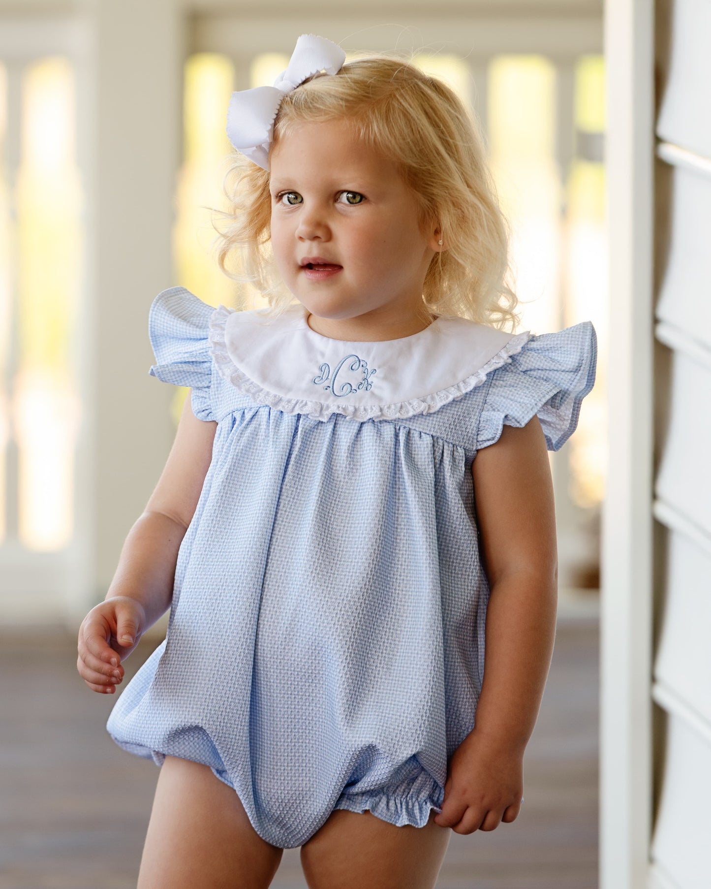 Young girl wearing a blue bubble with white ruffled collar indoors.