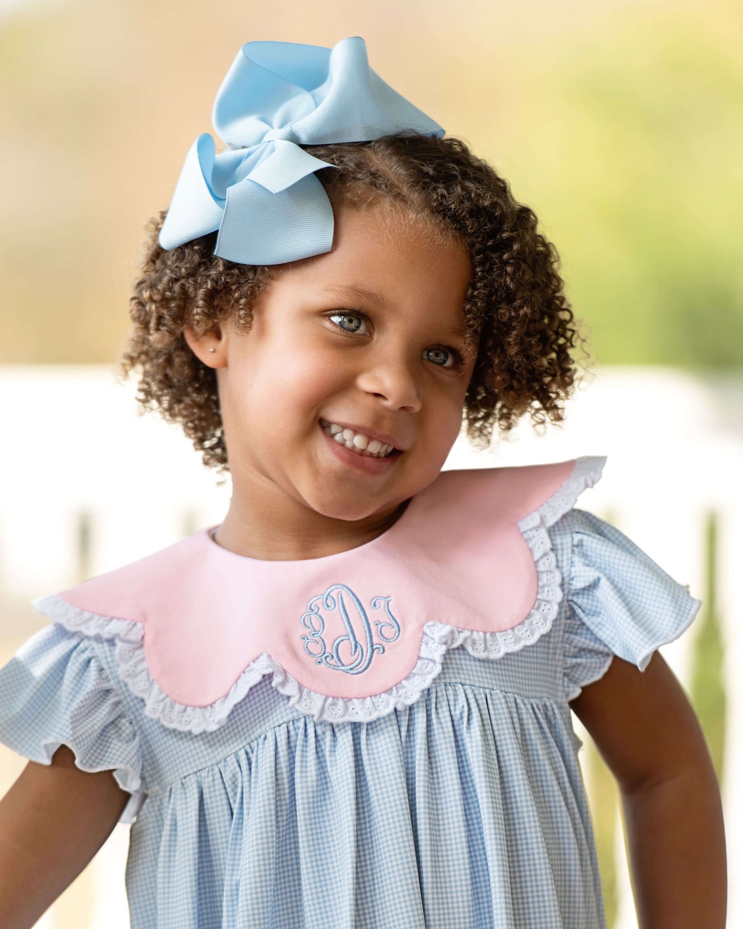Young girl wearing a blue dress with a pink collar and a large blue bow in her hair.