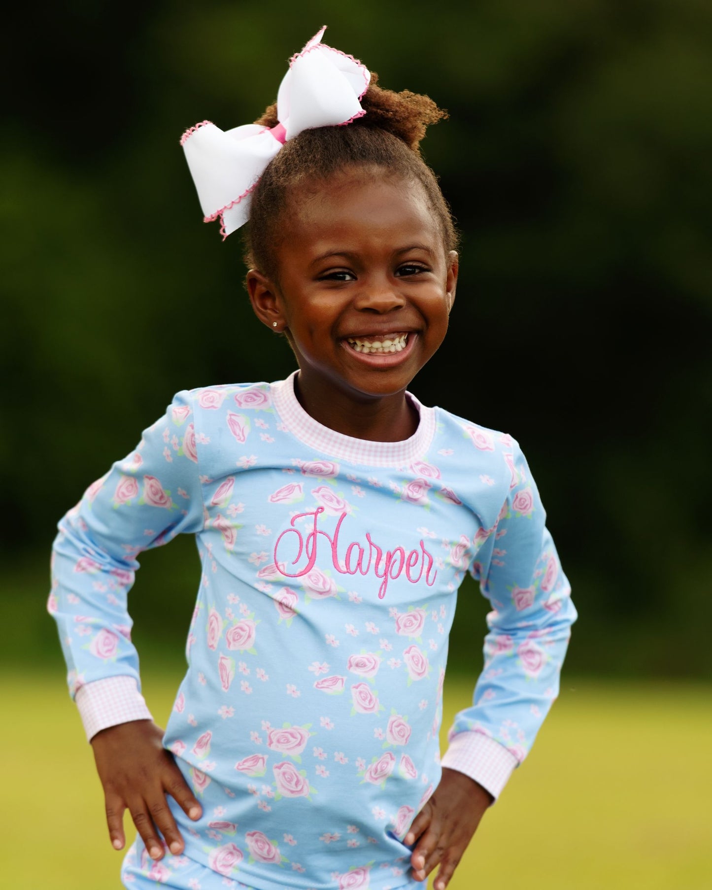 Young girl wearing a blue long-sleeve shirt with pink floral patterns and the name 'Harper' on it, standing outdoors.