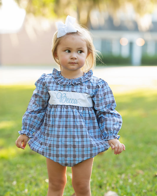 Young girl wearing a blue plaid dress with a name tag outdoors.
