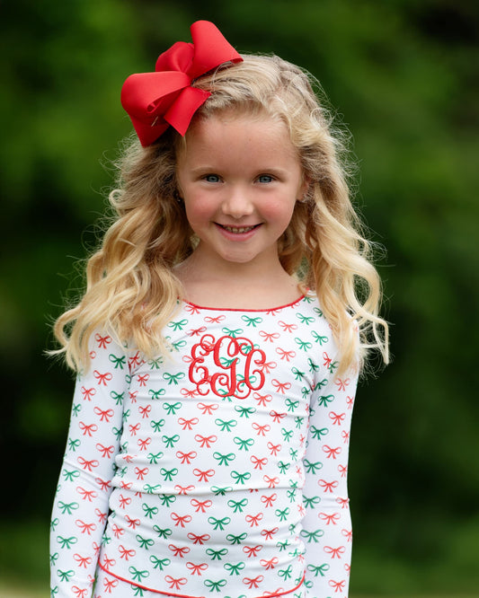 Young girl wearing a dress with a bow pattern and a red bow in her hair against a blurred green background