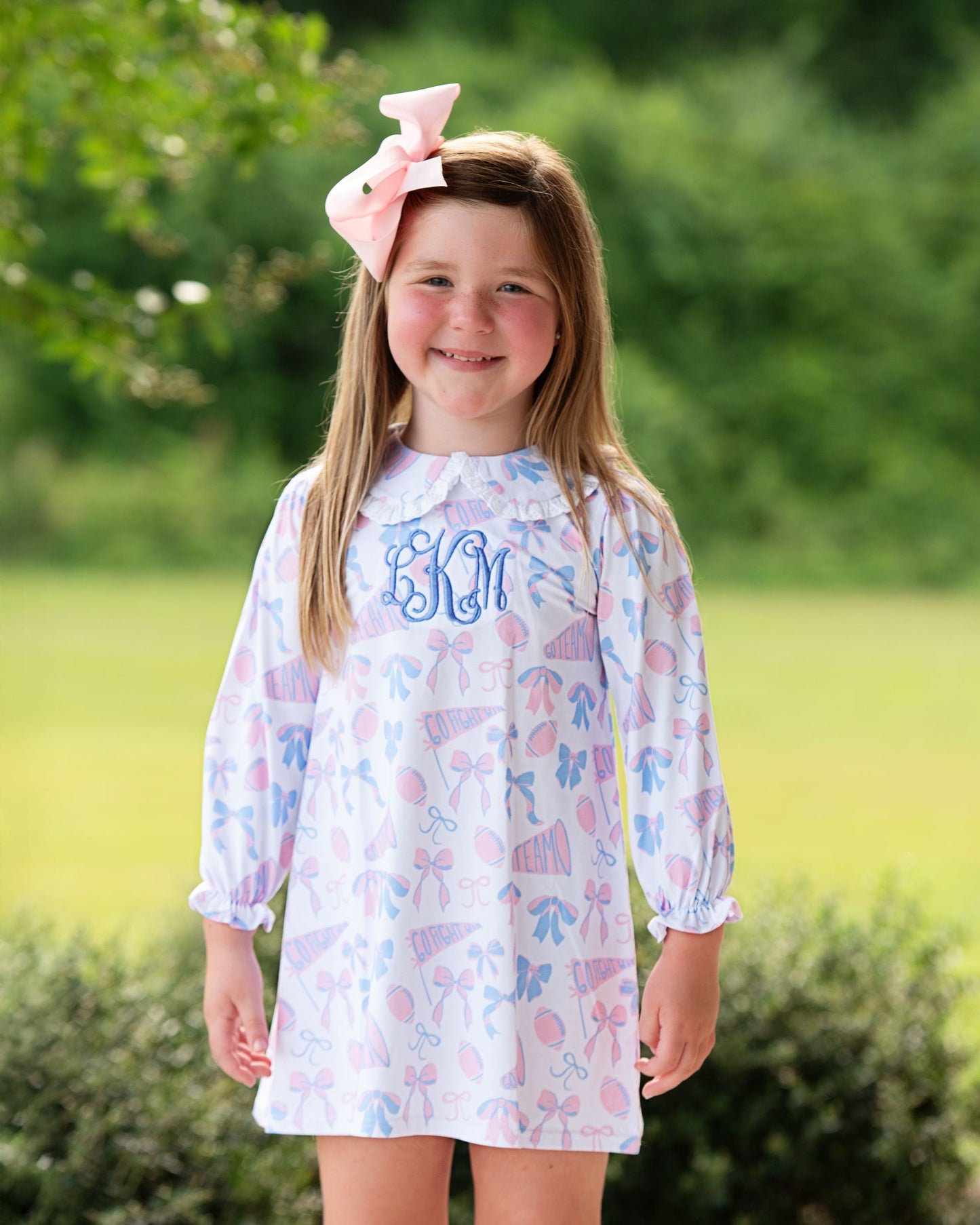 Young girl wearing a dress with butterfly pattern and 'BM' monogram outdoors.