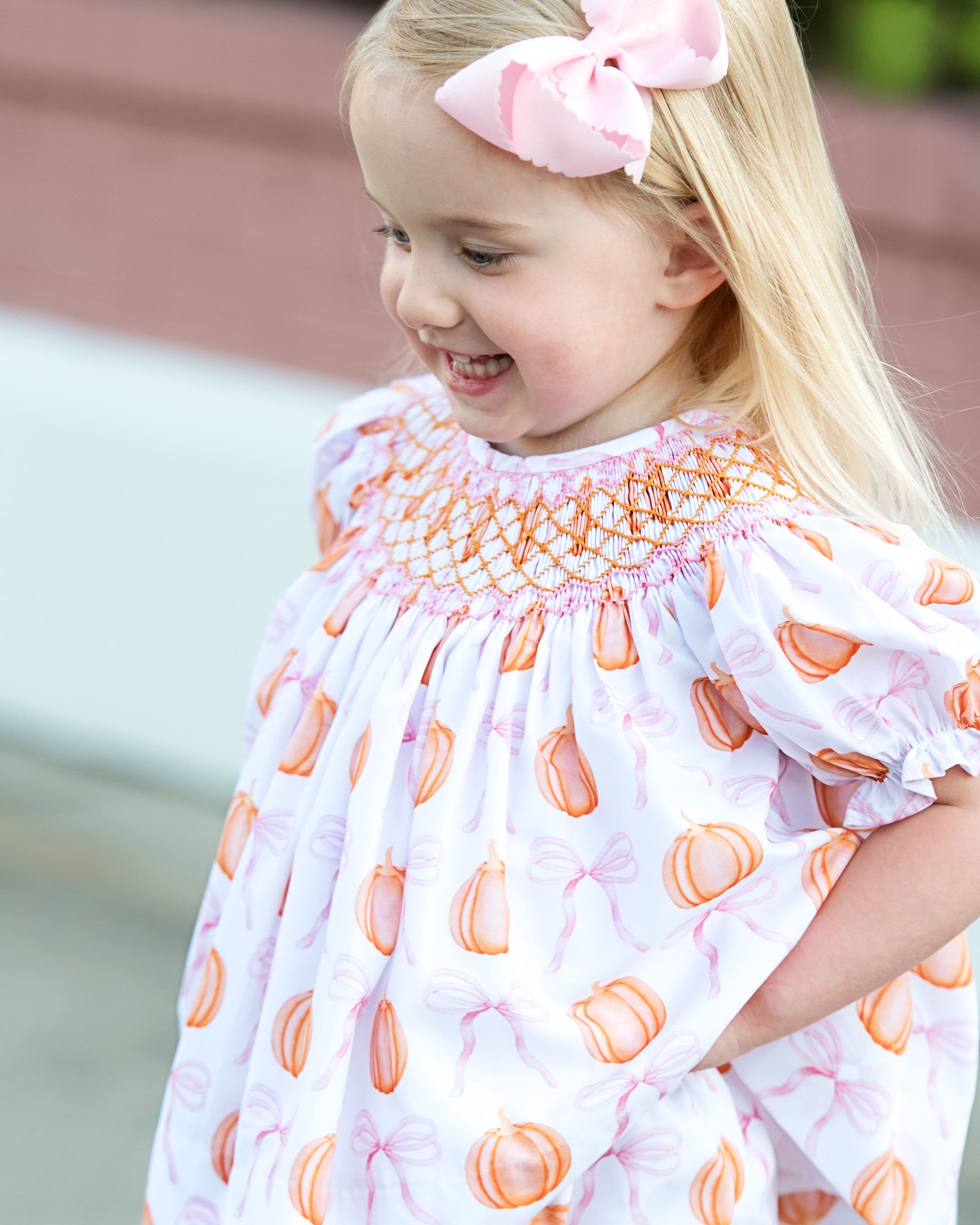 Young girl wearing a dress with orange pumpkins and pink bows patterns outdoors