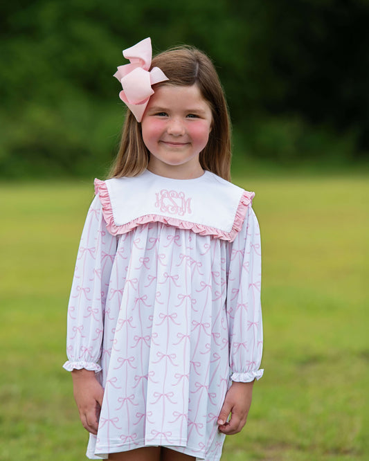 Young girl wearing a dress with pink bow details outdoors.