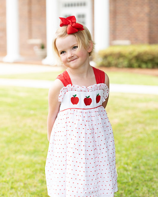 Young girl wearing a dress with smocked apples on it.