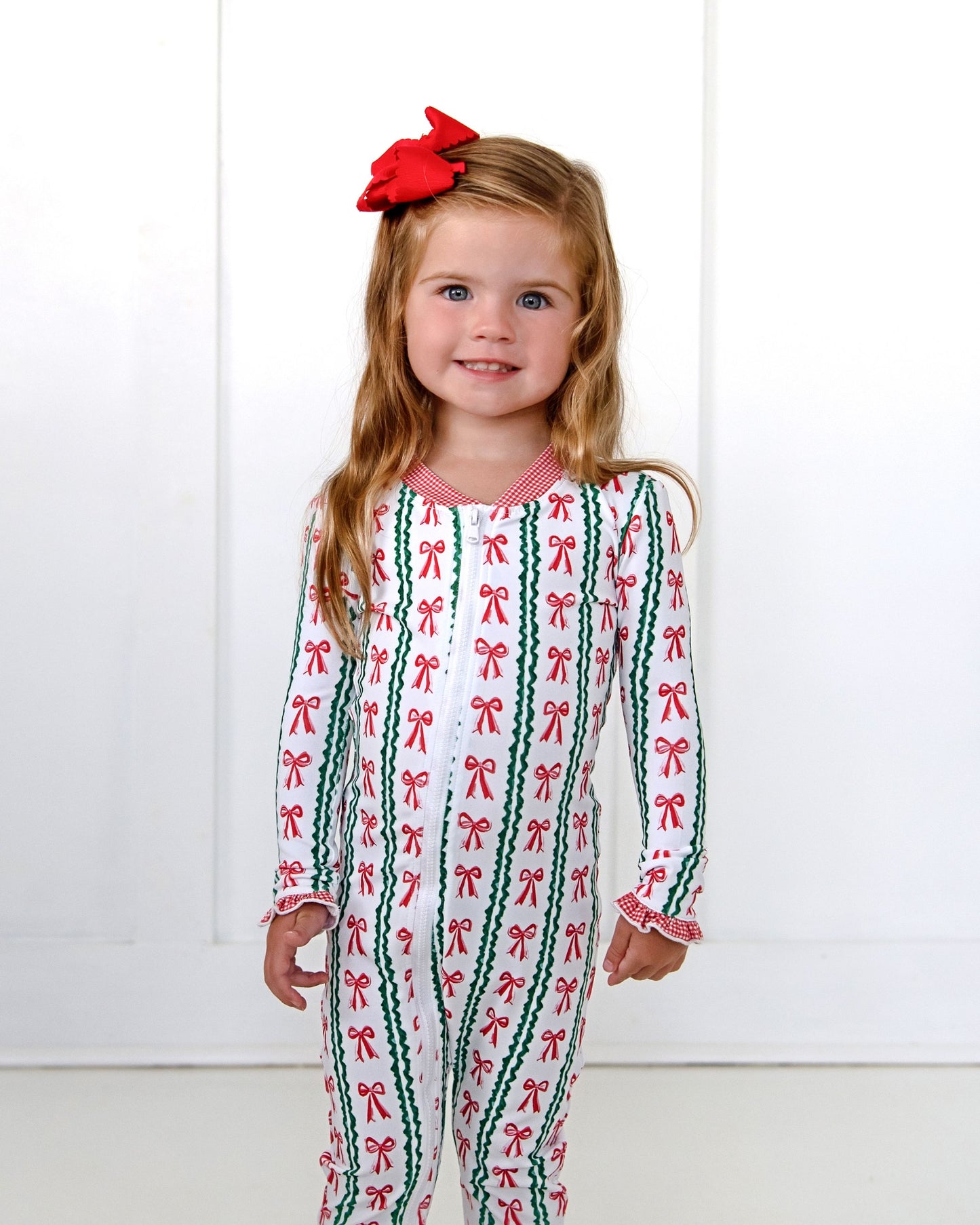 Young girl wearing a festive onesie with bow pattern against a white background