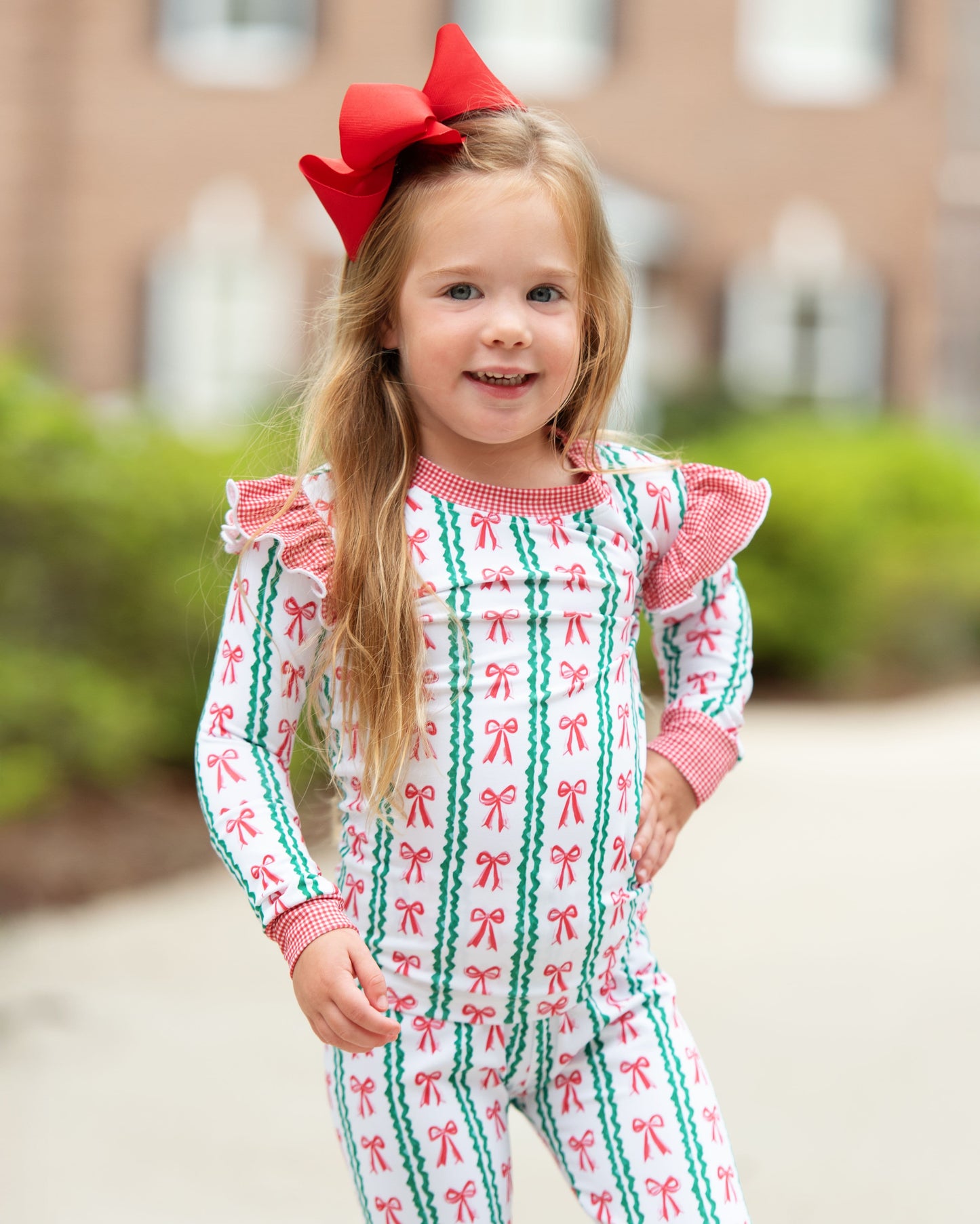 Young girl wearing a festive outfit with a red bow, standing outdoors.