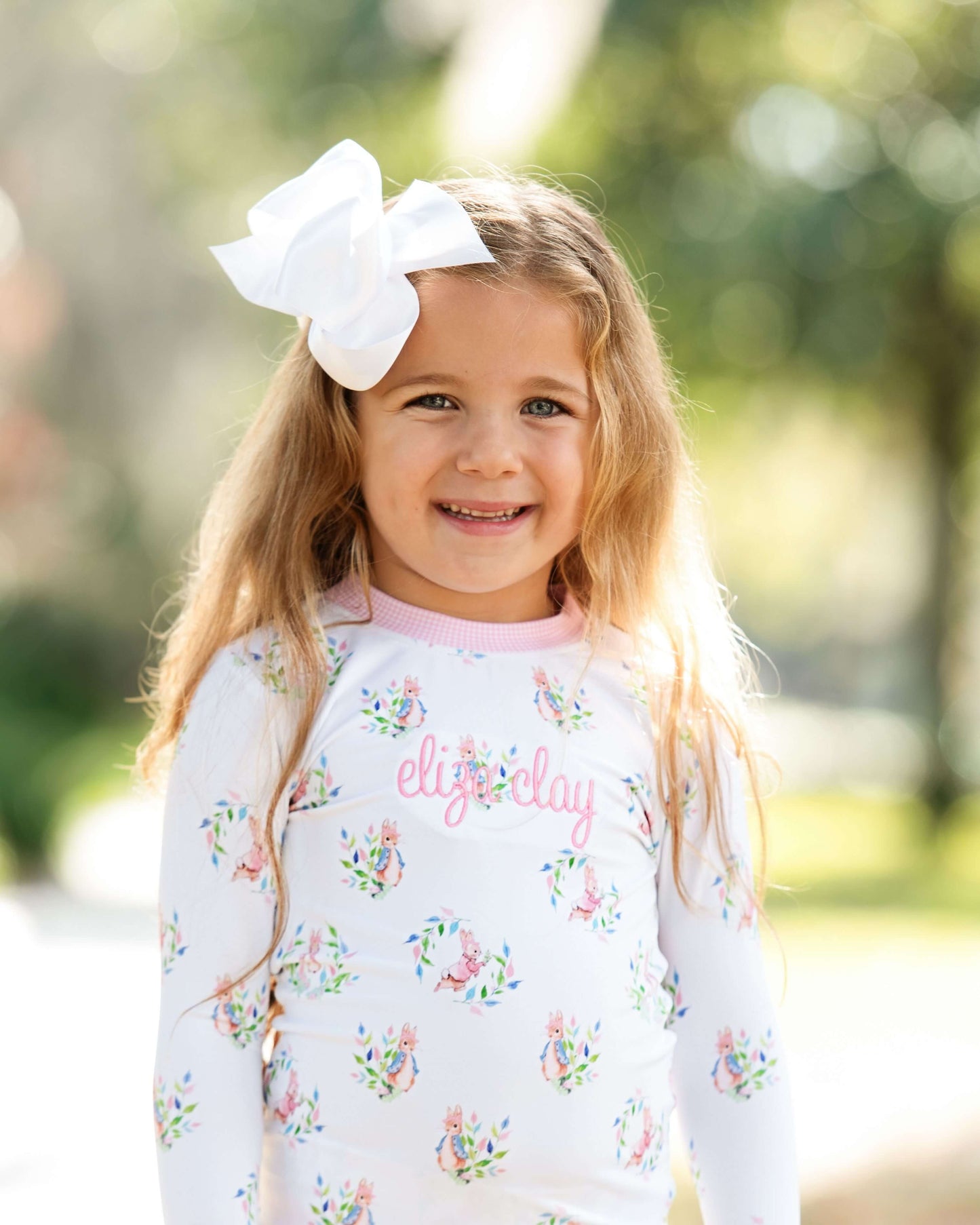 Young girl wearing a floral-patterned shirt with 'elise clay' printed on it, standing outdoors.