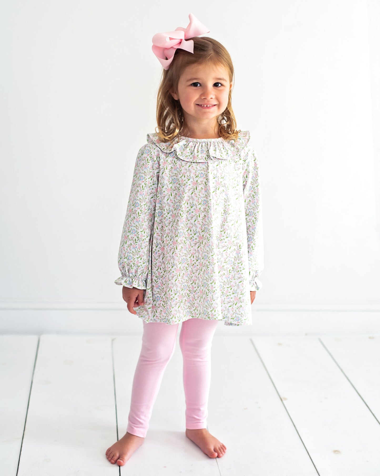 Young girl wearing a floral dress and pink leggings with a white background