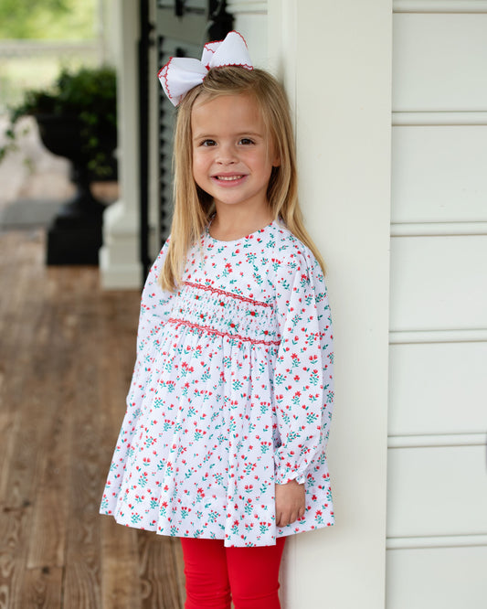 Young girl wearing a floral dress and red leggings standing on a wooden porch.