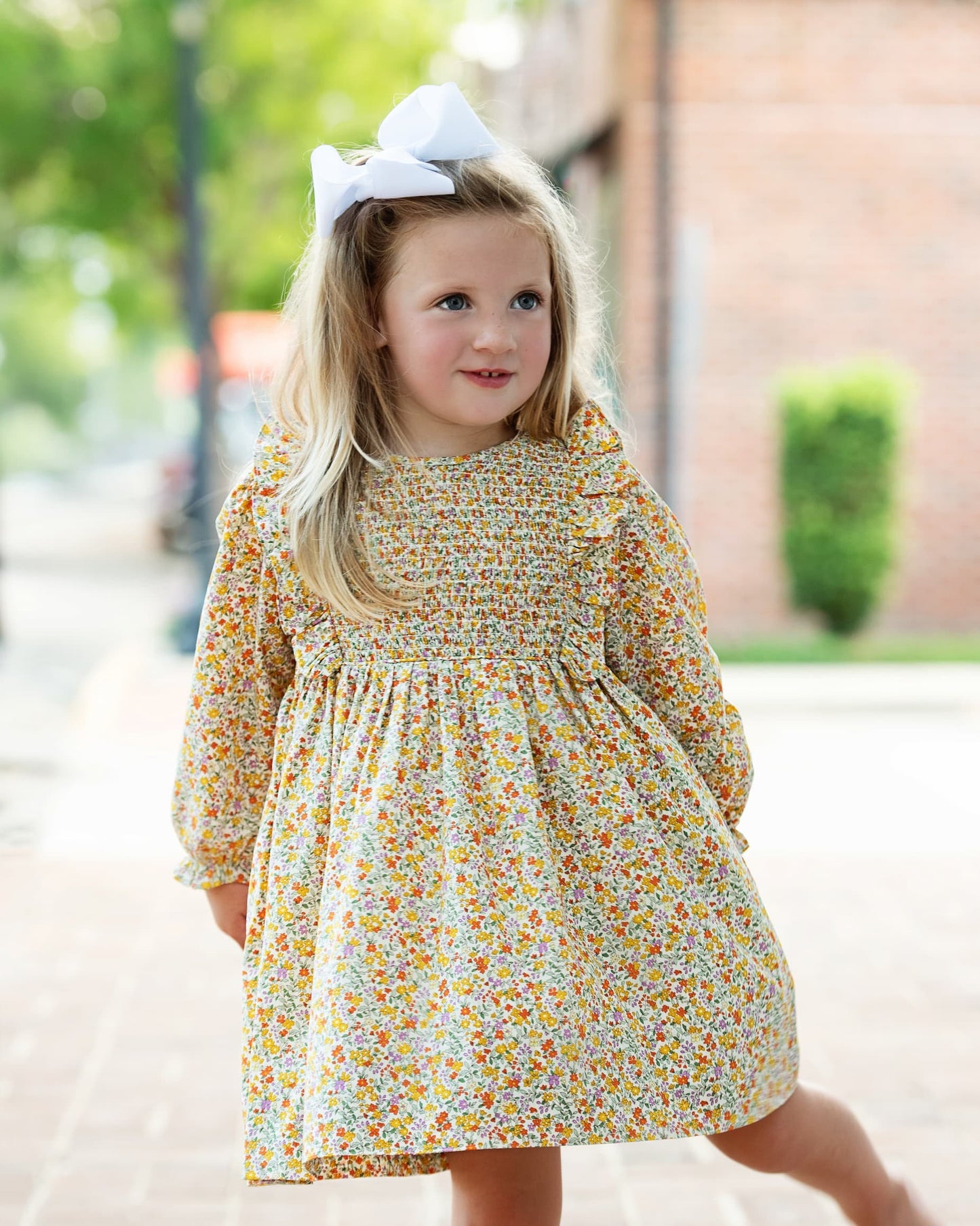 Young girl wearing a floral dress with a bow in her hair outdoors